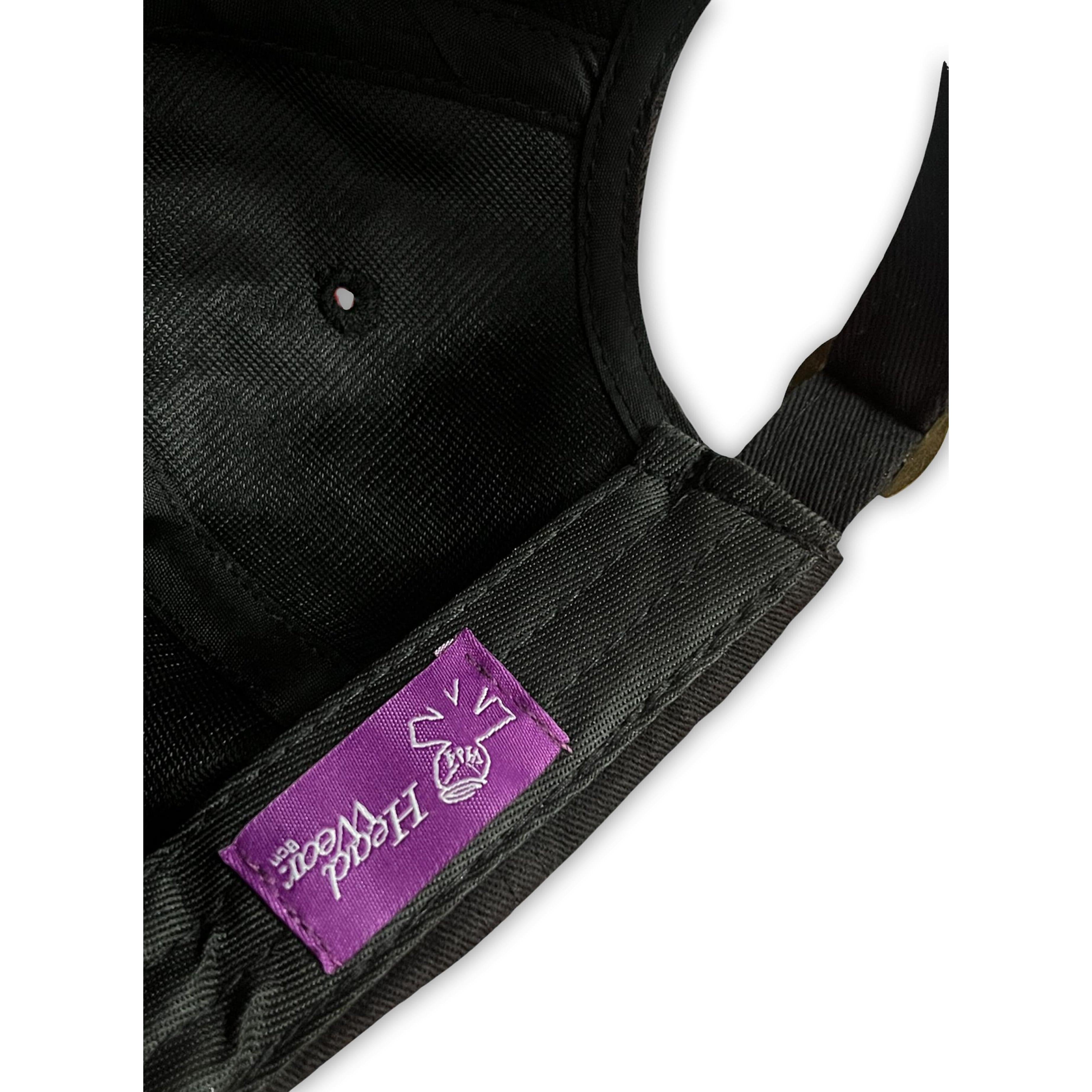 Close-up of the V1da The Dad Cap, a black unstructured hat with a purple stitched label featuring a white "HOOD WOOD" graphic and the word "BASK.