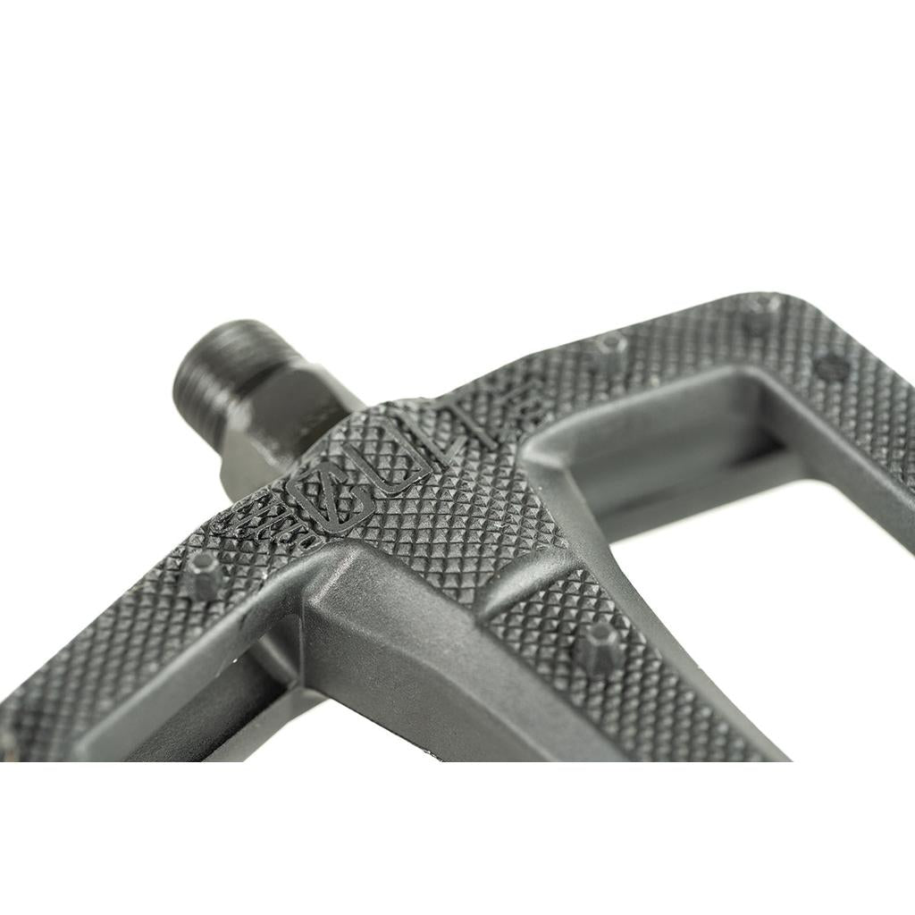 Close-up of the Cult Dak PC Pedal in textured black, featuring a metal spindle, detailed surface pattern, and part of the Dakota Roche signature molded marking.