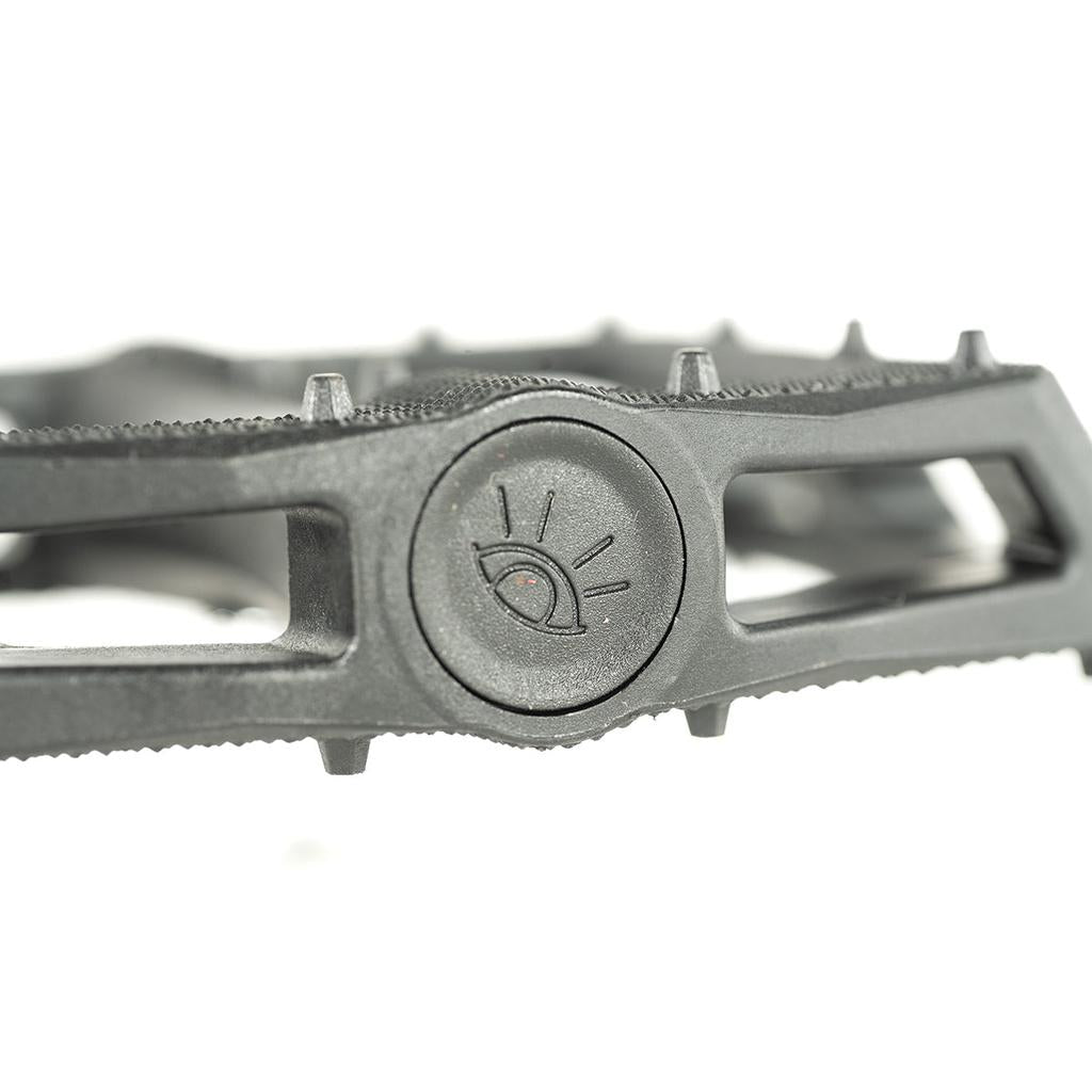 Close-up of the Cult Dak PC Pedal, a black BMX pedal with Dakota Roche's signature design, featuring an eye emblem at the center and a textured, ridged surface for enhanced grip.