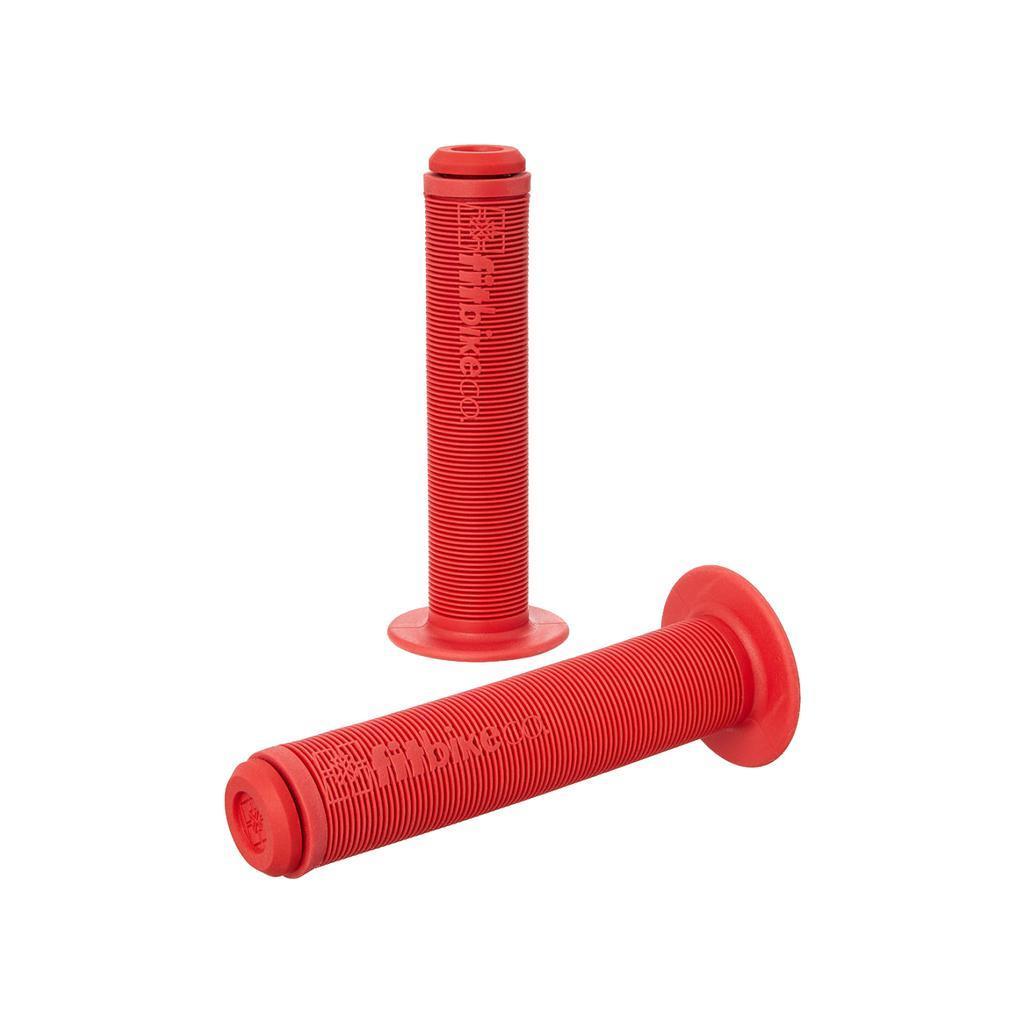Two red Fit Bike Co OG Grips with ribbed mushroom finned texture are shown—one standing upright, one lying down—both featuring flared ends and embossed branding.