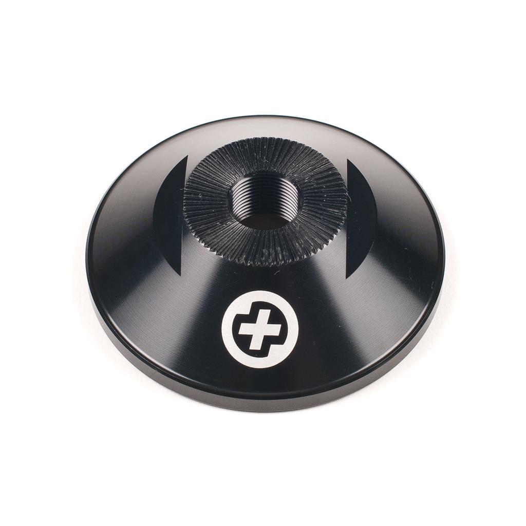 The Saltplus Trapez F/C Hubguard Alloy is a black 7075-T6 metal disc with a threaded center, two curved notches, and a white cross near the edge, made for TRAPEZ freecoaster hub setups and shown on a white background.