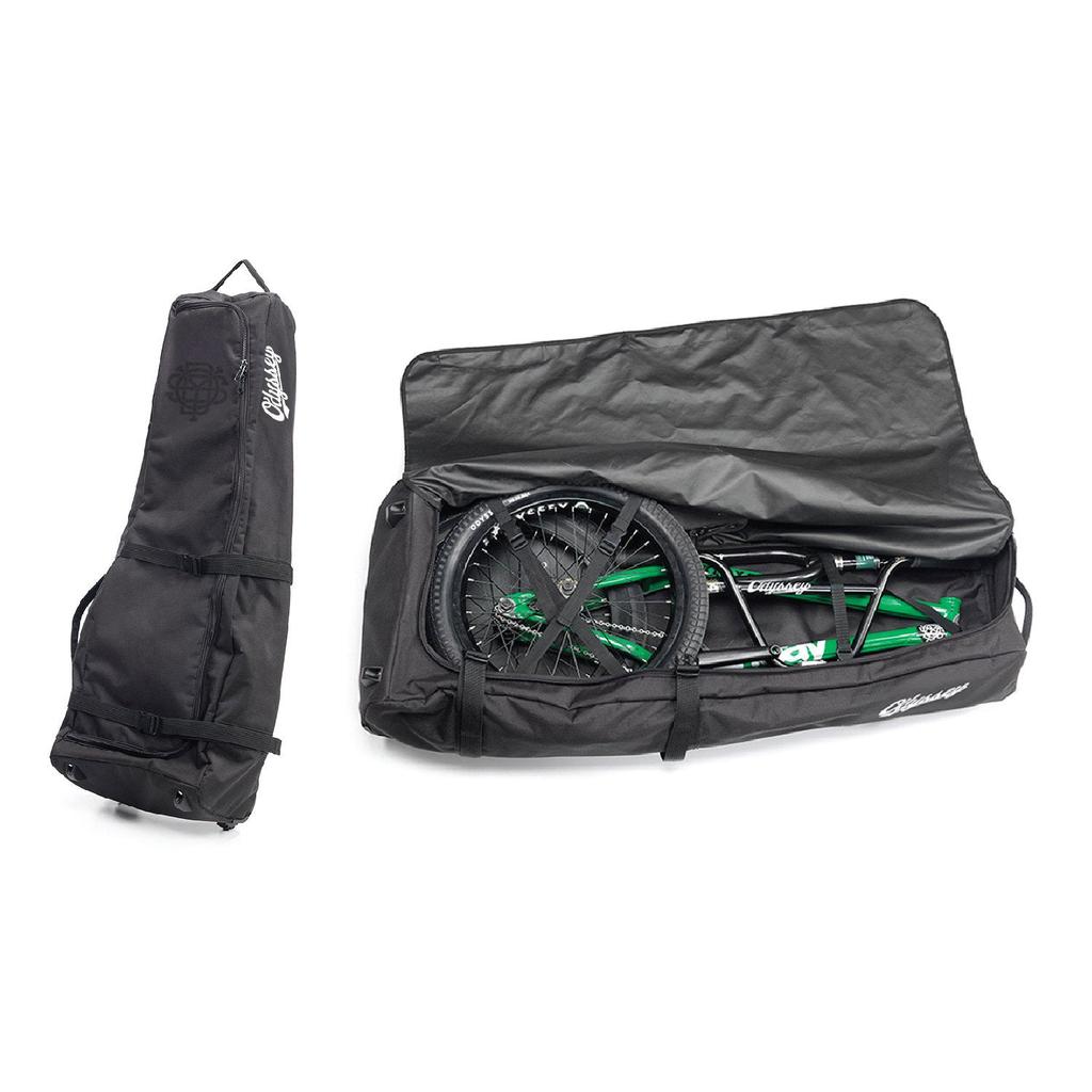 A bike is disassembled and packed in a sleek black Odyssey Monogram Bike Bag. Another matching bag stands upright on the left, zipped for your next adventure.