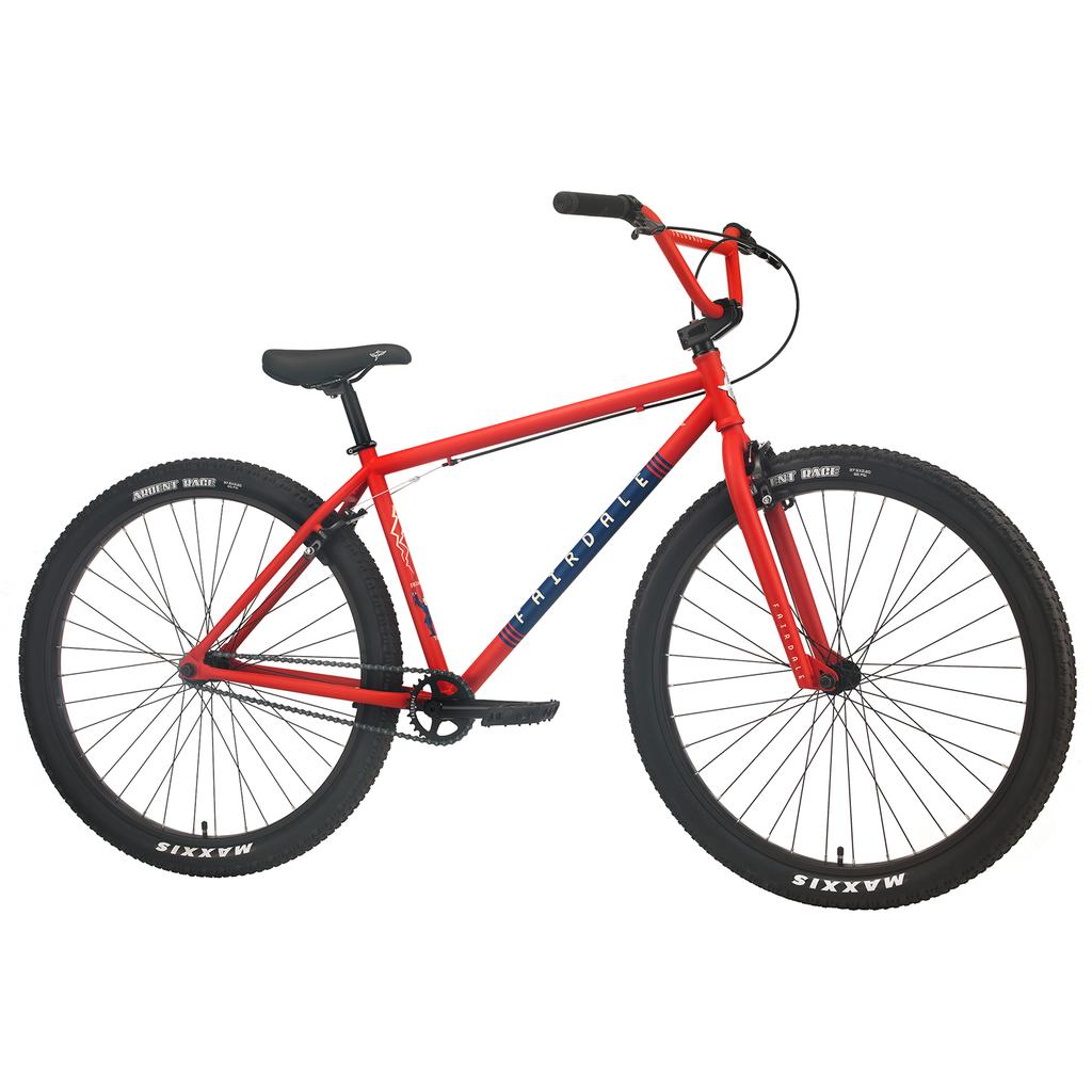 The Fairdale Taj 27.5 Inch Bike (2023) is a red BMX commuter with black tires and a blue diagonal stripe on the frame, shown from the side against a white background.