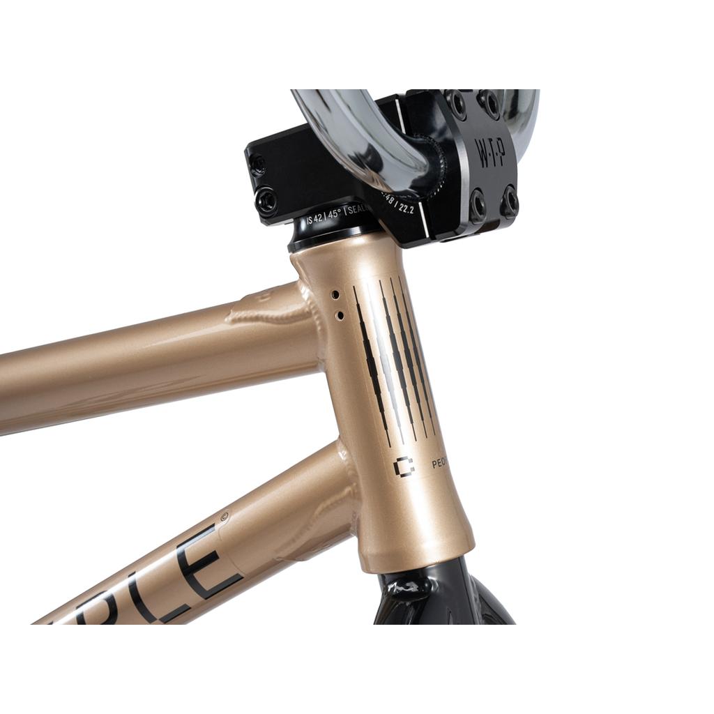 Close-up of the metallic bronze head tube with black decals, stem, handlebars, and partial logo—features of the Wethepeople Crysis 20 Inch BMX Bike equipped with Overbite Tyres for enhanced grip.
