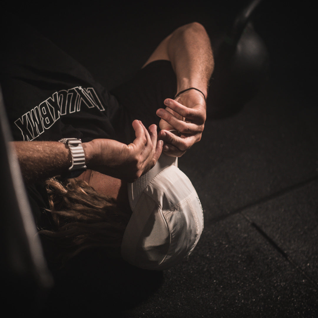 A man laying on the ground with a LUXBMX Bike Athletics T-Shirt - Black logo bandage on his head, wearing an Active Blend tee, drenched in sweat.