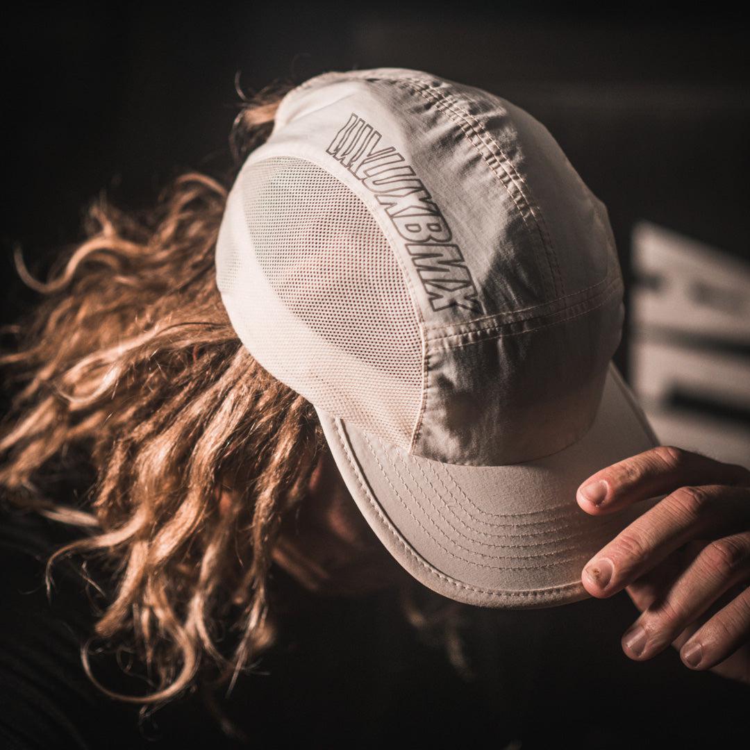 A man with long hair, wearing the LUXBMX Bike Athletics Cap - Ecru, shops at the BMX store and discusses how to pump his bike.