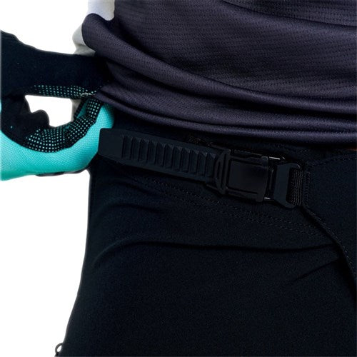 A person wearing a teal and black glove adjusts the waistband buckle of the TLD 26.1 Sprint Pro Pants / Mono Black, which are durable riding pants designed for comfort and flexibility with 4-way stretch fabric.