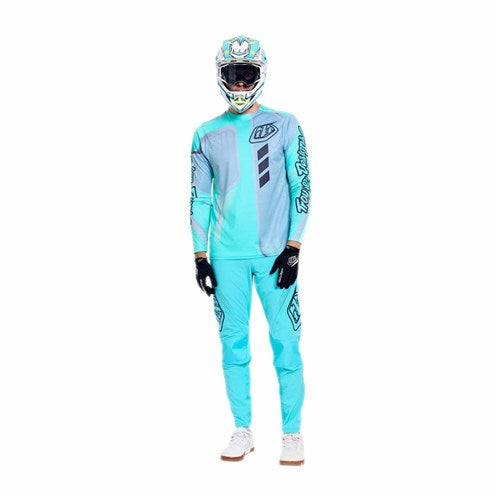 Person wearing TLD 26.1 Sprint Pro Pants / Mono Real Teal, a light blue and teal motocross outfit with durable 4-way stretch pants, helmet, gloves, and white shoes, standing against a plain white background.