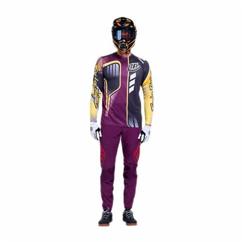 A person wearing TLD 26.1 Sprint Pro Pants / Mono Sangria, made from 4-way stretch fabric, along with a helmet, goggles, gloves, and a long-sleeve jersey stands facing forward against a plain white background.