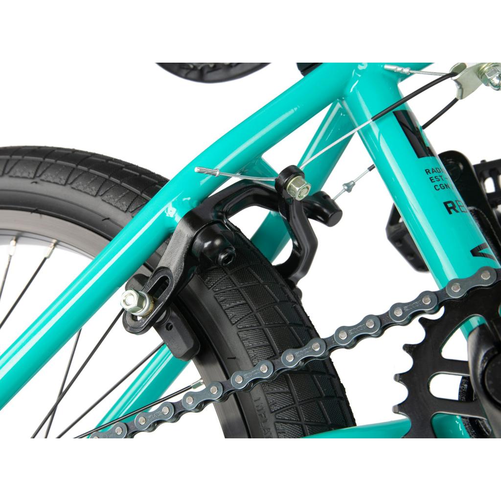 Close-up of the Radio Revo Pro FS 20 Inch Bike's teal BMX rear wheel, highlighting the brake mechanism, tire tread, chain, and part of the gear system on its 20-inch frame.