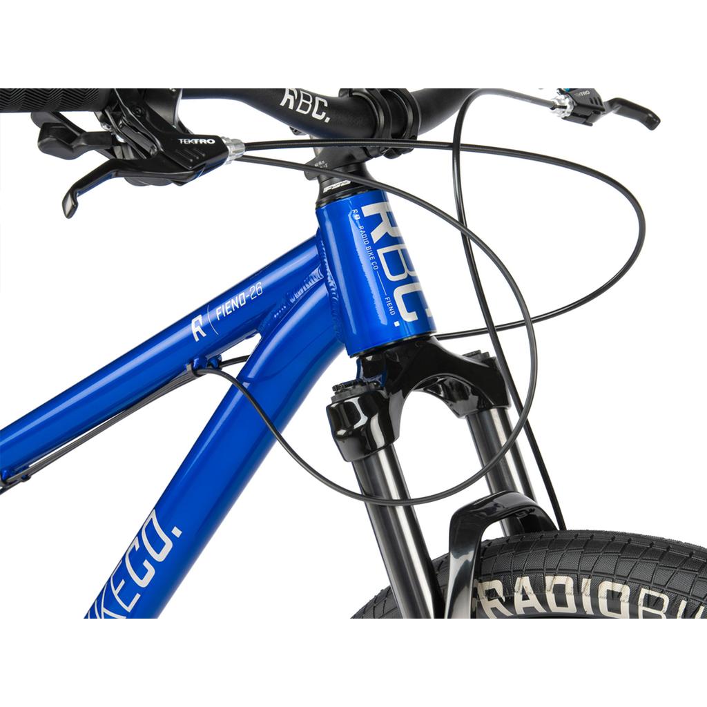 Close-up of the blue Radio Fiend 26 Inch Bike, featuring its handlebars, fork, cables, and part of the front tire labeled "RADIO," all constructed on a durable 6061-T6 alloy frame.