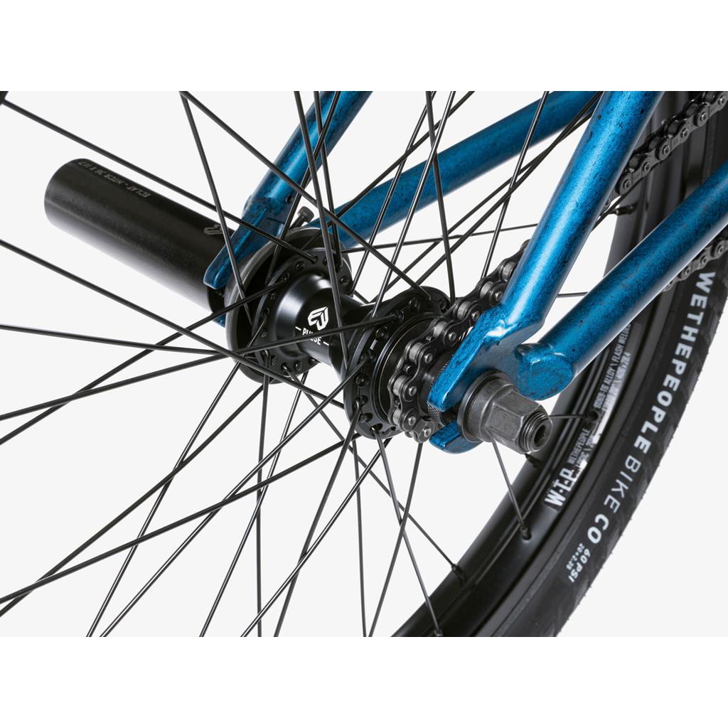 Close-up of the rear wheel hub, chain, black axle peg, and tire showing the "WeThePeople Bike Co" brand on the Wethepeople Revolver 20 Inch Bike, known for its high-quality aftermarket parts.
