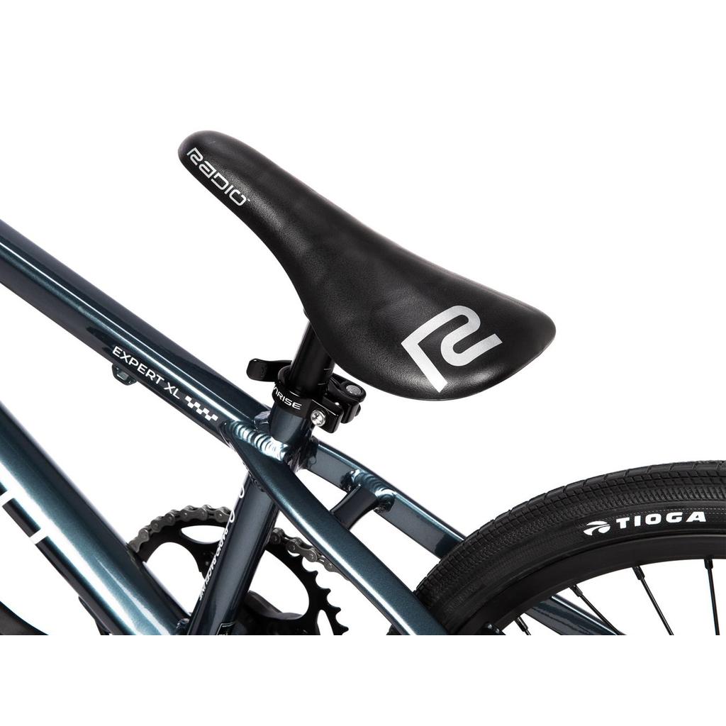 Close-up of the Radio Xenon Expert XL Disc 20 Inch Bike seat labeled "Radio," displaying the seat post, frame, part of the rear wheel, and a Tioga-branded tire against a white background. The image highlights the bike’s lightweight alloy frame and pro-level components designed for high-performance BMX racing.