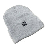 The Profile Woven Label Beanie, a light gray knit beanie featuring a black "Profile Racing" woven label, is displayed on a wooden surface, highlighting its quality and union-made craftsmanship.