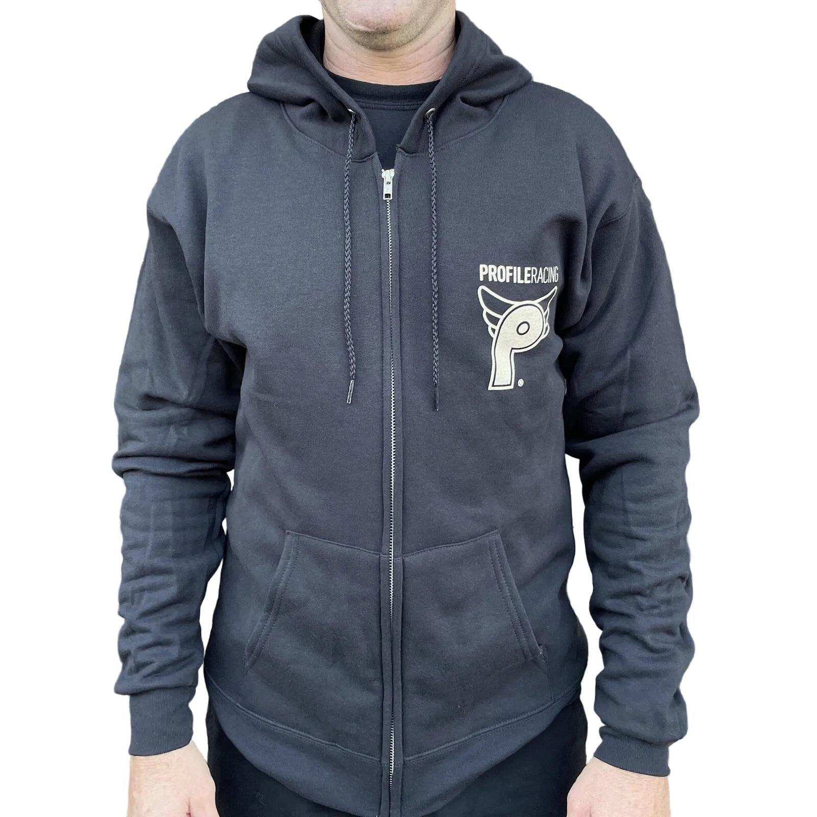 Person wearing a black Profile From the Dungeon Zip Hoodie with "Profiler Racing" logo on the left chest, standing by a fence with plants in the background.