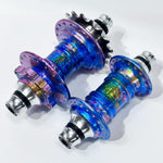 The Profile Mini Front & Rear Hub Set (LE-Galaxy Rust) for disc brakes, featuring a vibrant iridescent finish, is displayed side by side on a white background—a striking hubset for any bike build.