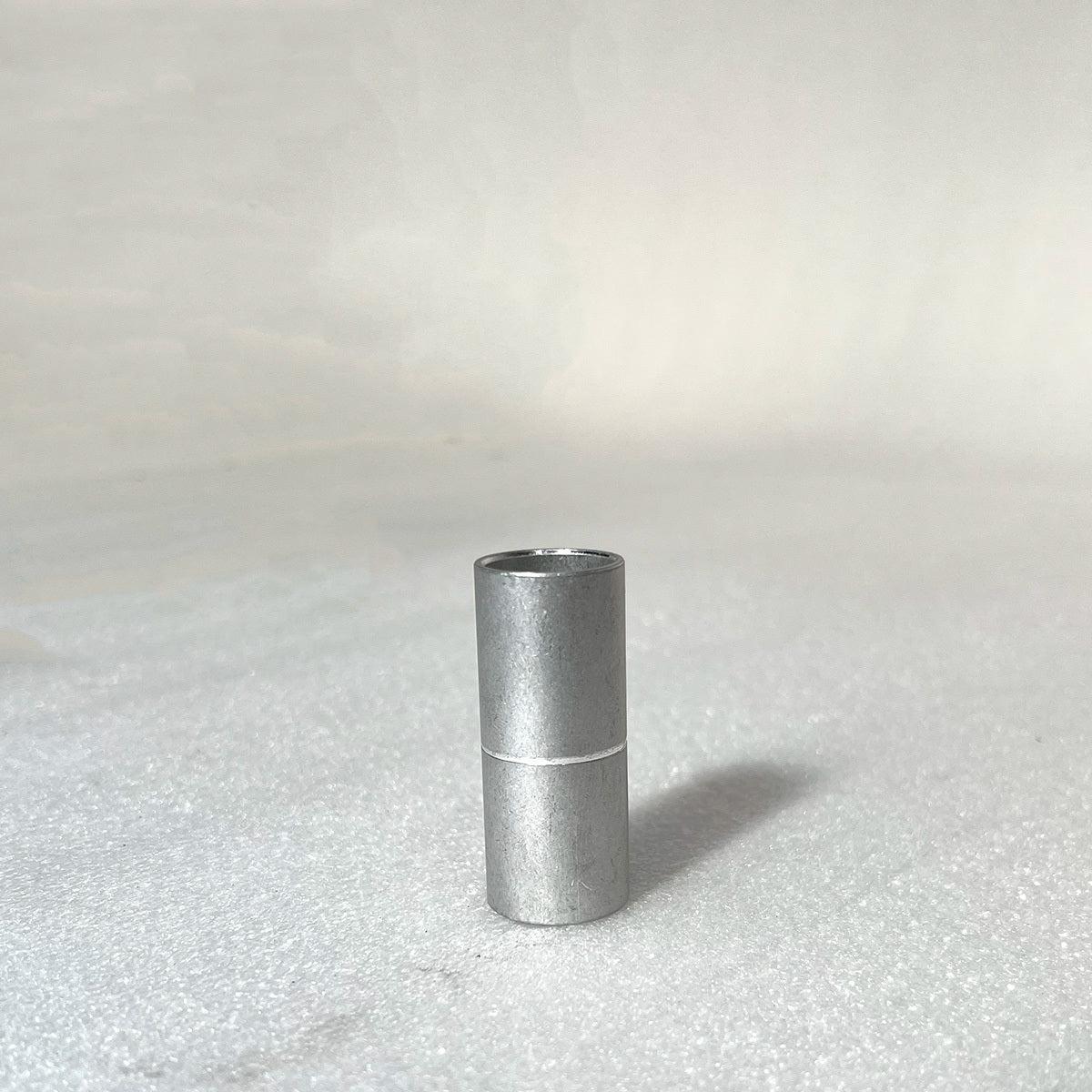 A small, cylindrical metal piece, resembling the Profile 19mm Tube Spacer (53mm), stands upright on a light textured surface.