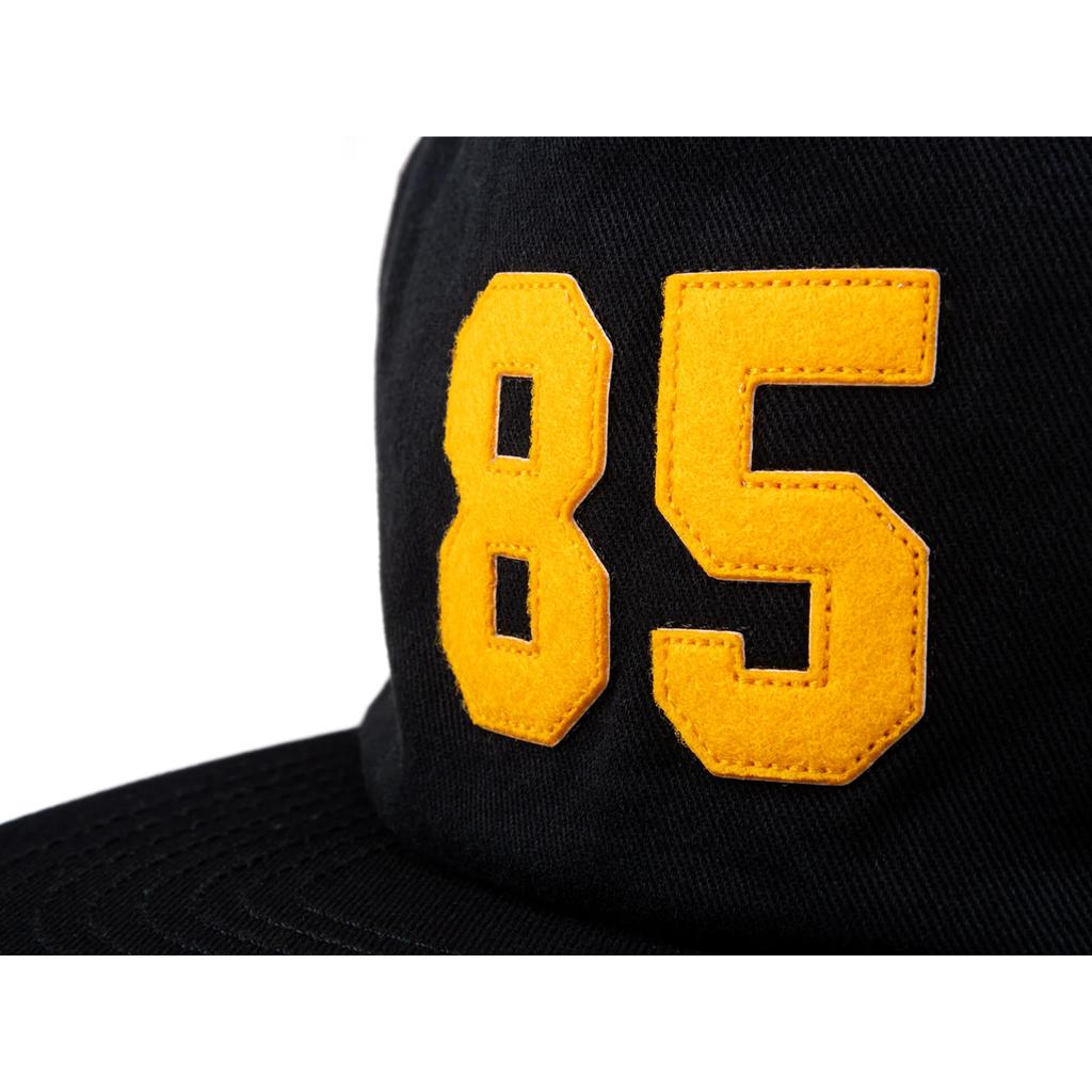 Close-up of the Odyssey 85 Cap, a black 5 panel hat with bold yellow "85" stitching—ideal for Back to School 2025.