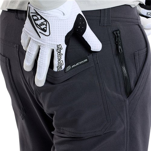 A person in black TLD 25.2 Ruckus Long Travel Pants / Mono Carbon puts a gloved hand into the back pocket while wearing a white, black, and gray Taylor R glove.