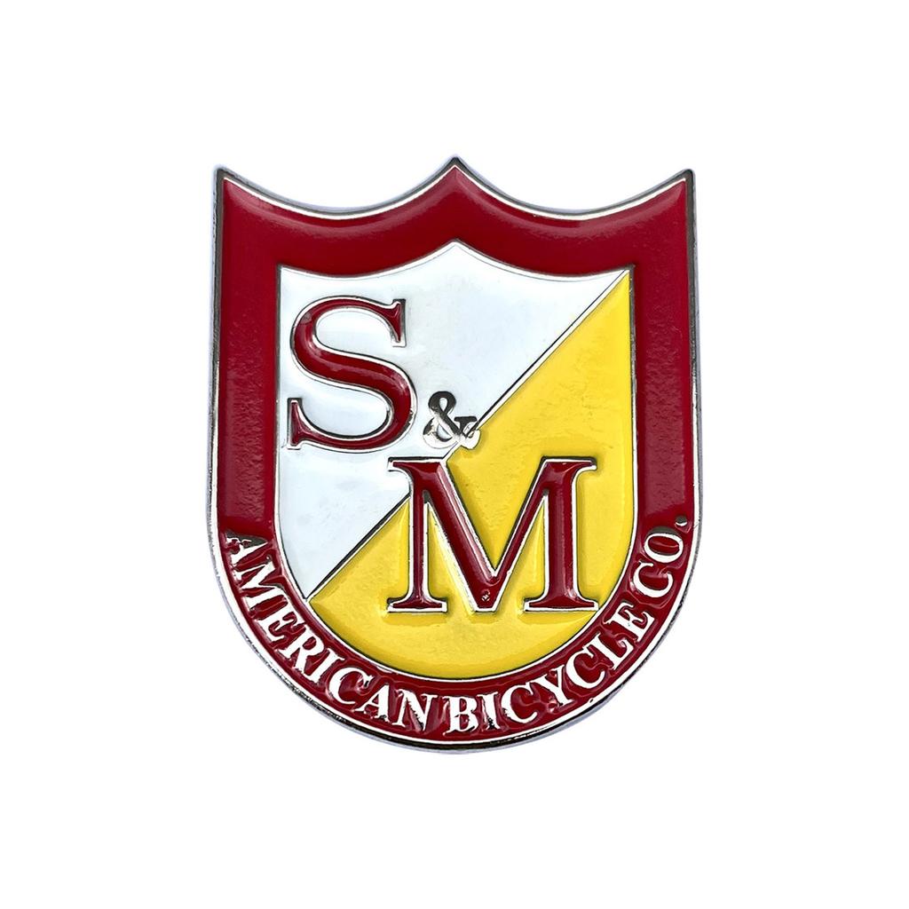 The S&M Shield Pin, featuring a red and yellow shield logo with "S & M" and "American Bicycle Co." text, adds flair and captures the spirit of adventure in an enamel pin design.