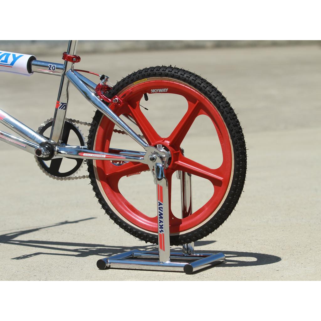 Close-up of a bicycle’s rear wheel with red spokes, supported by the Skyway Stolz Stand on a concrete surface.