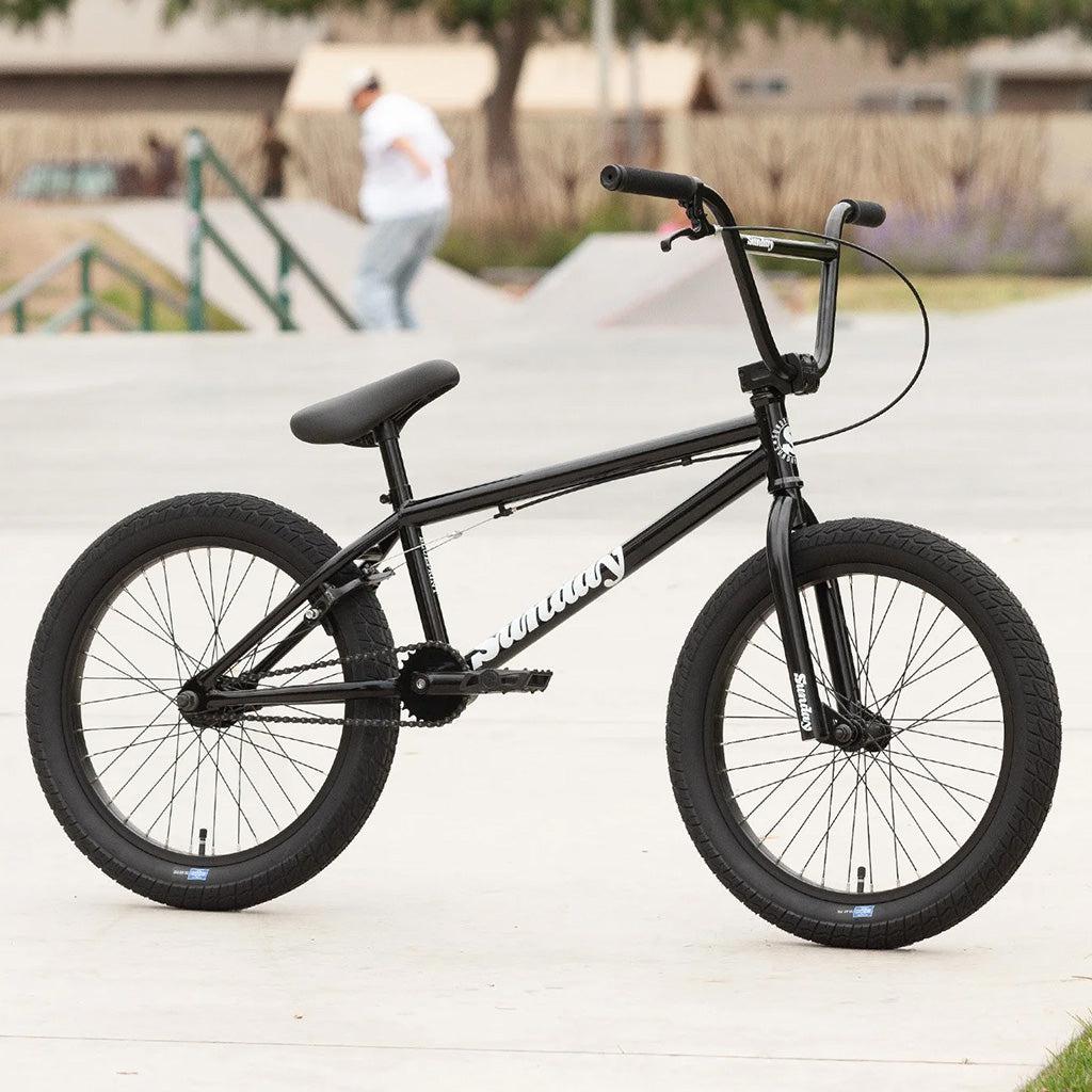 A beginner's black BMX bike, the Sunday Blueprint 20 inch Bike, parked on a sidewalk.