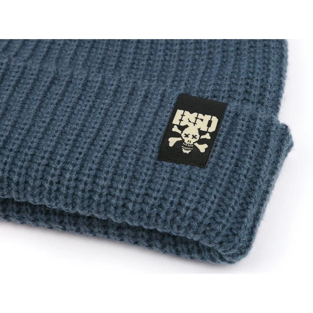 A close-up of the BSD More Speed Beanie, a blue wide knit hat featuring a black patch with a white skull, crossbones, and "HSD" text.