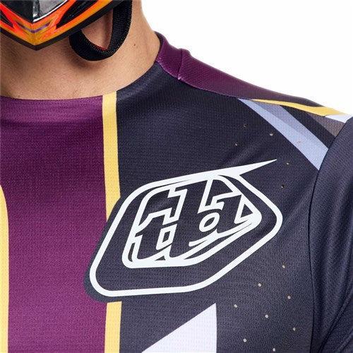 Close-up of a person wearing the TLD 26.1 Sprint Pro Jersey / Lowrider Sangria, featuring moisture-wicking fabric, a white "tld" logo, and part of a helmet visible at the top.