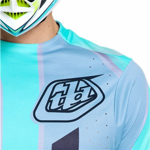 A person wears the TLD 26.1 Sprint Pro Jersey / Lowrider Real Teal, featuring teal and blue colors with the "TLD" logo on the chest; a helmet is partially visible at the top of the image.