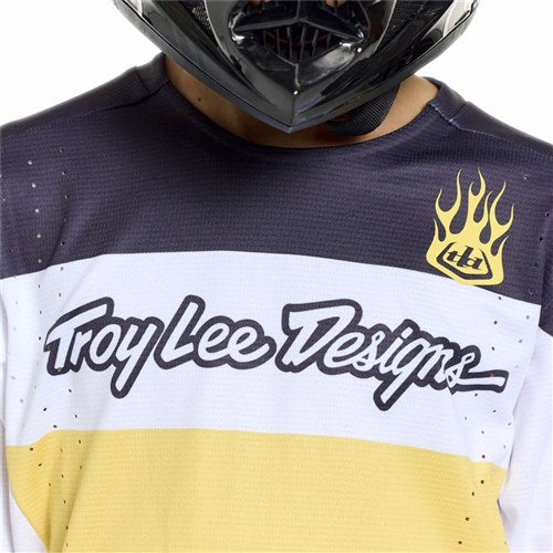 A person wearing a black helmet and a TLD 26.1 Sprint Pro Jersey (Youth) / Yo Moto Butter, which features a yellow flame logo on the upper right chest.