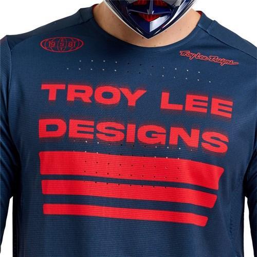 Person wearing a TLD 25.2 Sprint Jersey / Segment Midnight, featuring blue fabric with red text and stripes, along with a partial view of a helmet.