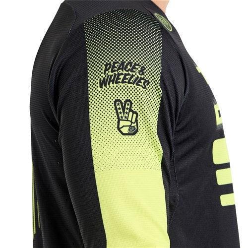 A close-up of the TLD 25.2 Sprint Jersey / Segment Black sleeve by Troy Lee Designs, showing "PEACE & WHEELIES" text and a peace sign hand graphic in black and yellow.