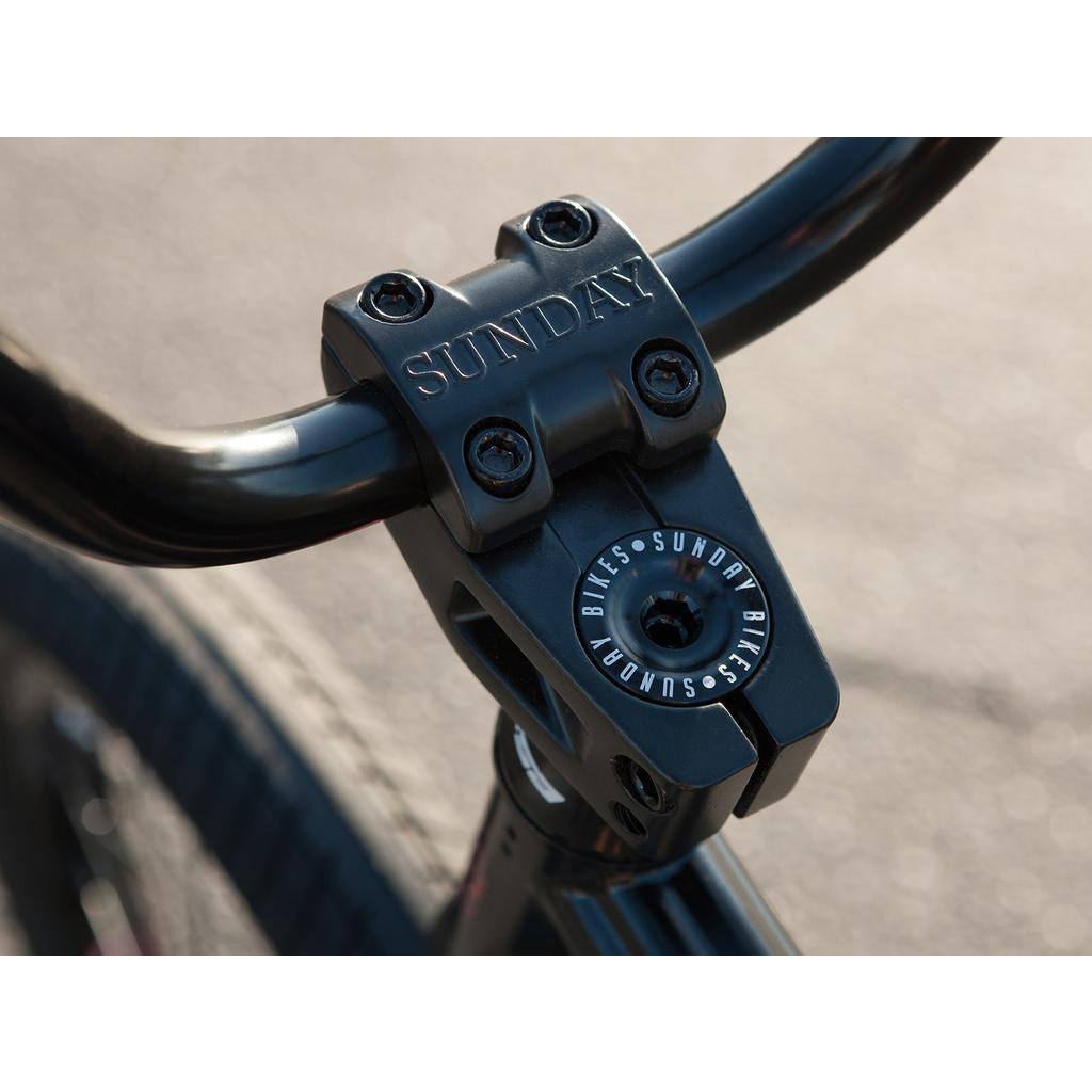 Close-up of the black stem on the Sunday Sound Wave Special 20 Inch Bike (2023), with "SUNDAY" engraved on top and "SUNDAY BIKES" printed around the center bolt, featuring quality Odyssey parts.