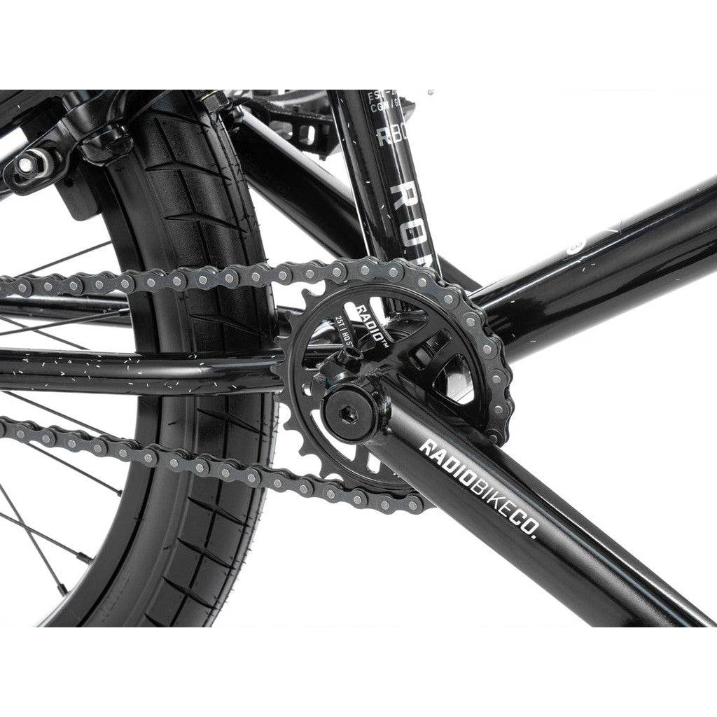 Close-up of a black bicycle's drivetrain, featuring a chainring, chain, and rear tire. The crank arm displays the brand name "Radiobike Co." This Radio Astron FS 20 Inch Bike also boasts Radio Pro Hubs for enhanced performance.