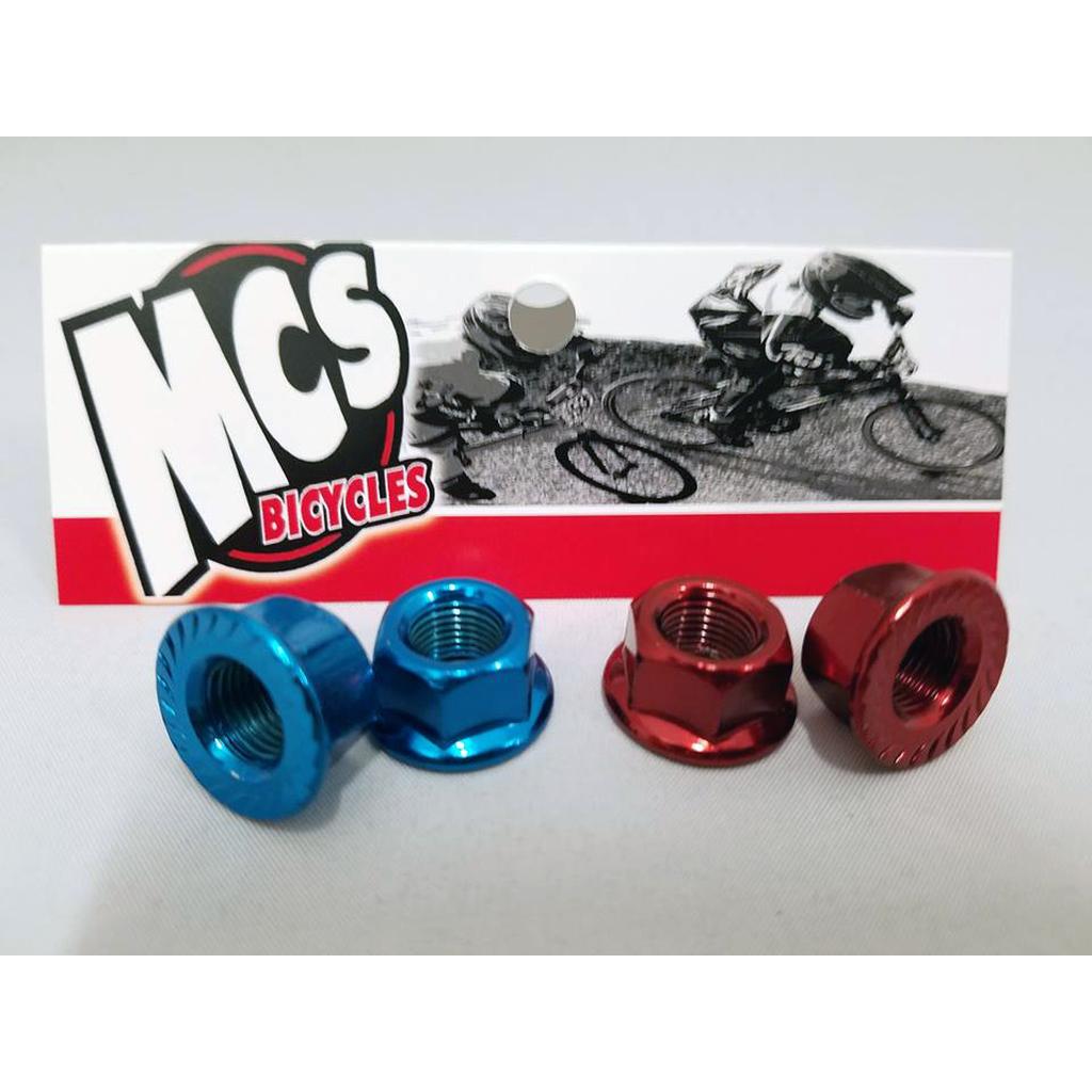 Two pairs of MCS Axle Nuts (3/8" 26TPI), one pair in blue and one in red, are displayed in front of an MCS Bicycles card showing cyclists racing.