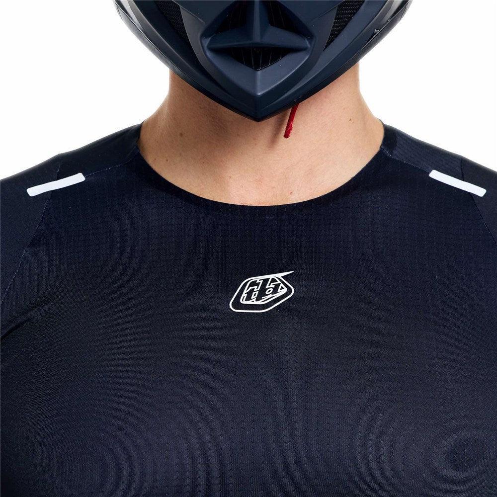 Person wearing a TLD 26.1 Sprint Ultra Jersey / Mono Black from Troy Lee Designs, with a white chest logo and black helmet, shown in a shoulders-up photo.