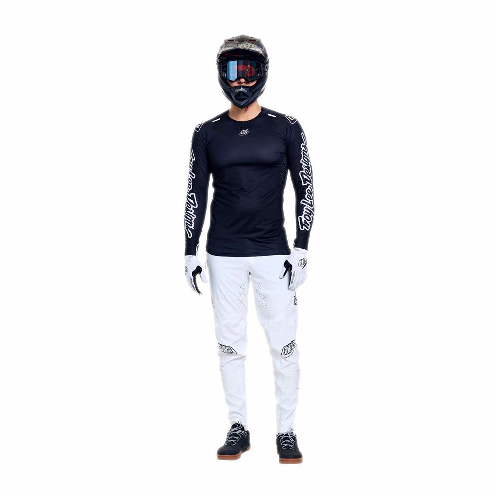 Person wearing a TLD 26.1 Sprint Ultra Jersey / Mono Black long-sleeve, white motocross pants, gloves, black shoes, and a full-face helmet with goggles, standing against a plain white background.
