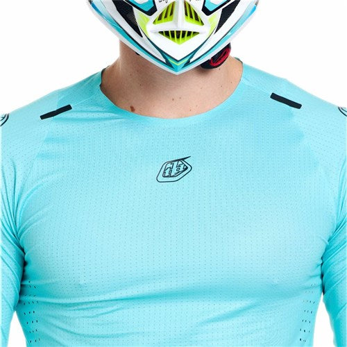 A person wearing the TLD 26.1 Sprint Ultra Jersey in Mono Real Teal and a colorful helmet, shown from shoulders to mouth, with only the lower half of the helmet visible.