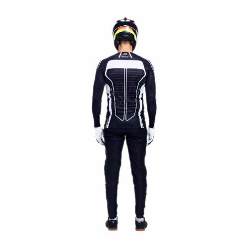 A person in black and white motorcycle gear, featuring the TLD 26.1 Sprint Ultra Jersey in Proton Black, stands facing away with arms at their sides against a plain white background.