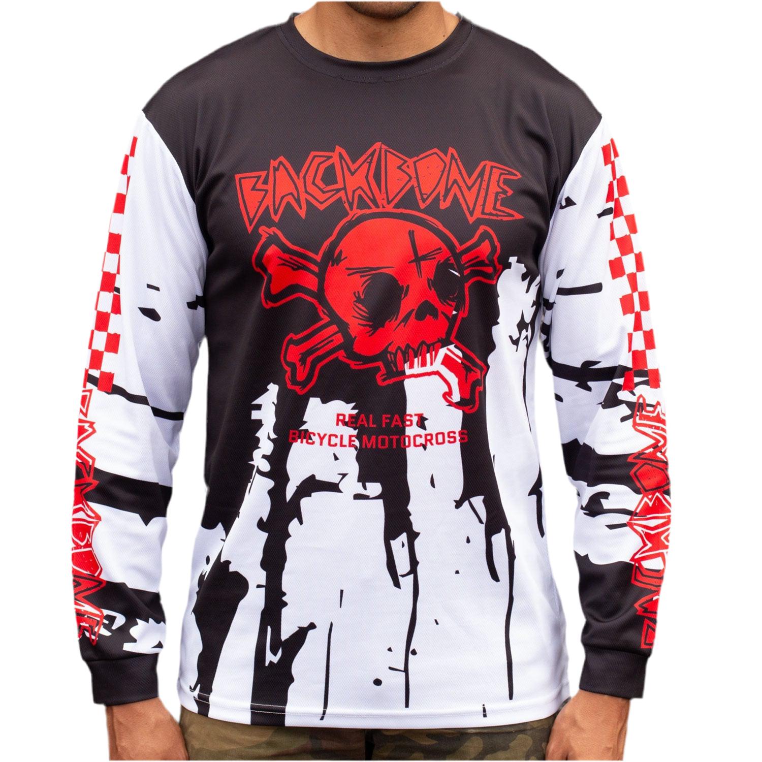 A man confidently wears the Backbone Real Fast Race Jersey / Gnar Drip (Youth), a long-sleeve shirt with a red skull and text design, crafted from 160 GSM polyester. It combines edgy style and BACKBONE FIT, reminiscent of sick jerseys with a unique twist.