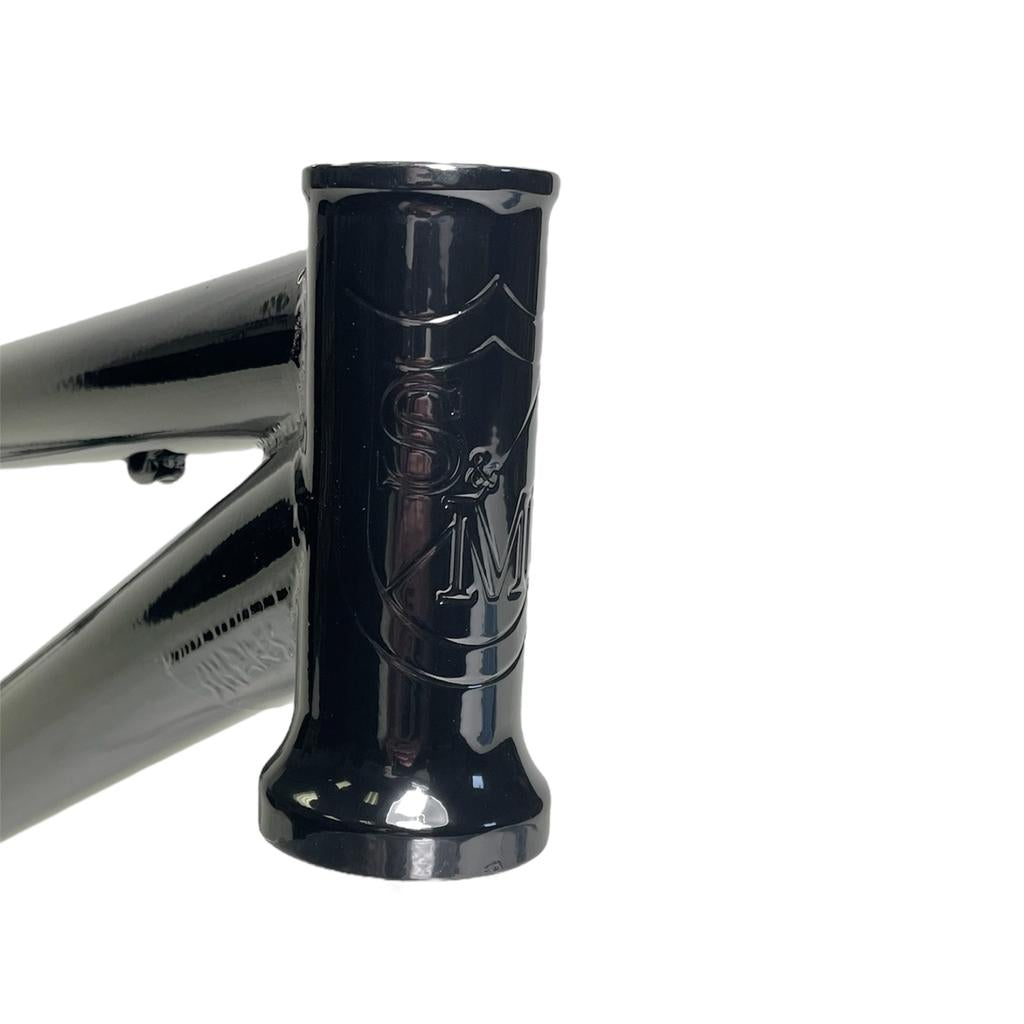 Close-up of the S&M Big Jumper V2 26 Inch Dirt Jumper Frame's black head tube, featuring an embossed shield logo with “S” and “M”; designed for a suspension fork and disc brake.