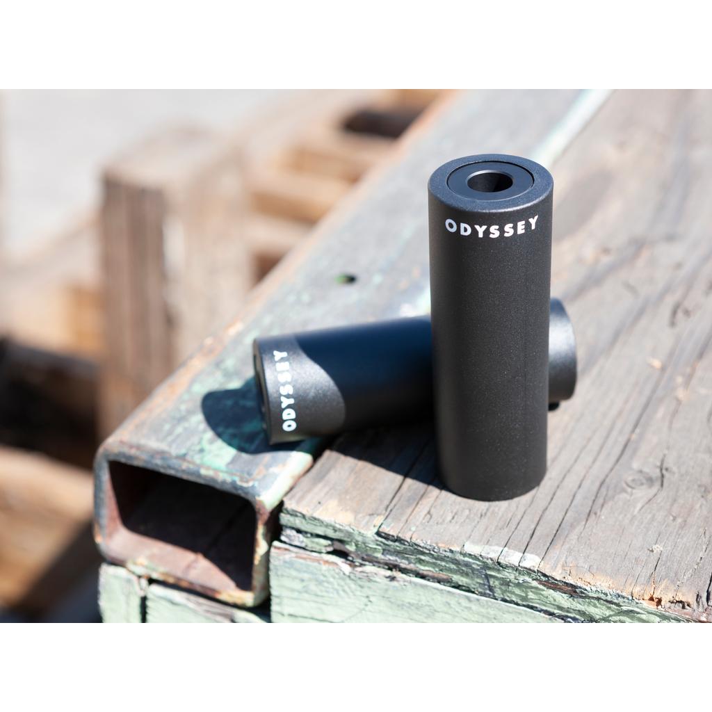 An Odyssey Joystick PC Peg (Each) with a lightweight aluminum core rests on a weathered wooden surface outdoors, one upright and one lying down—durable, stylish plastic pegs ideal for demanding riders.