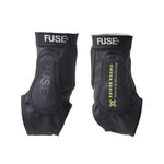 A pair of black Fuse Omega Pro Ankle Guards with padding, SAS-TEC impact protection, and "OMEGA SERIES PROTECTION SYSTEMS" printed in yellow on one guard.