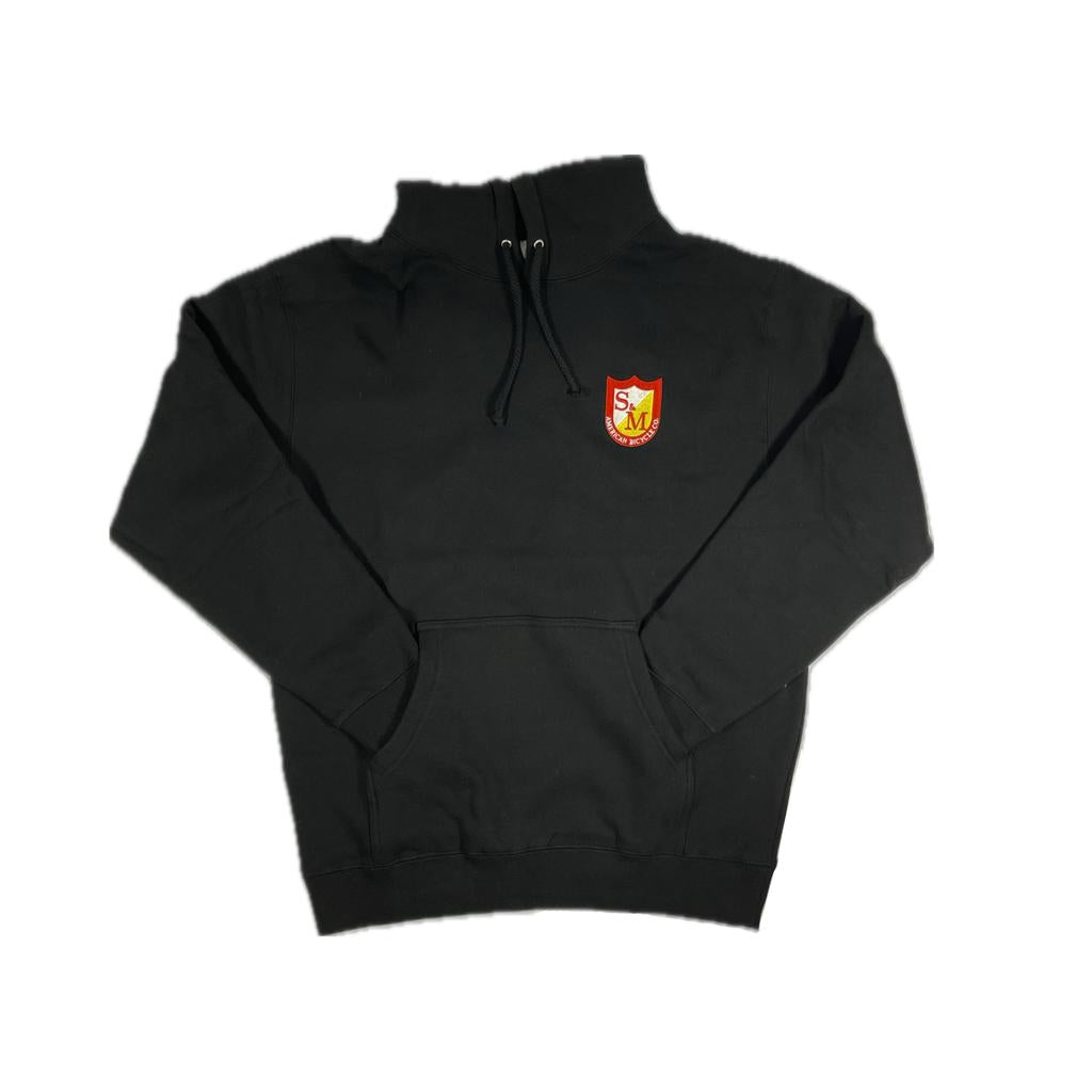 The S&M Shield Pullover Hoodie is a black, premium heavyweight style featuring a front pocket and a red and yellow "SM" crest shield on the left chest. Made from ring-spun cotton with a cozy fleece-lined hood.