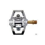 Close-up of HT Components - T2Ti Pedals featuring a black and silver body with a gold spindle, highlighting their lightweight design and excellent mud-shedding abilities against a white background.