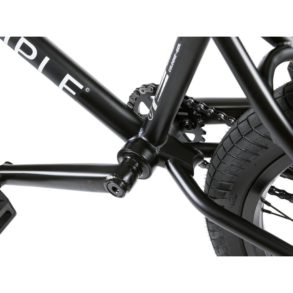 Close-up of the Wethepeople Crysis 20 Inch BMX Bike’s crankset, chain, pedal, and rear wheel, highlighting the frame, SaltPlus Ultra Three Piece Cranks, chainring, and Overbite Tyres’ rugged tread pattern.