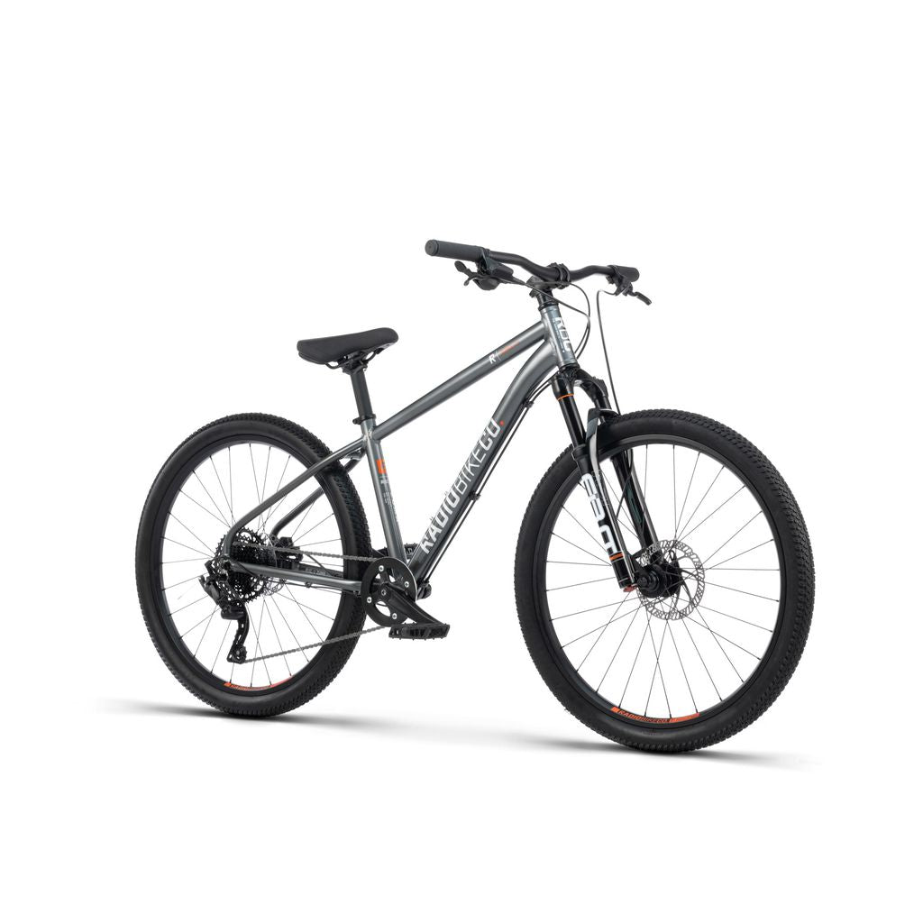 A lightweight, kid-sized MTB, the Radio 26 Inch Zuma Sus Bike, with front suspension, disc brakes, and knobby tires is on display against a white background.