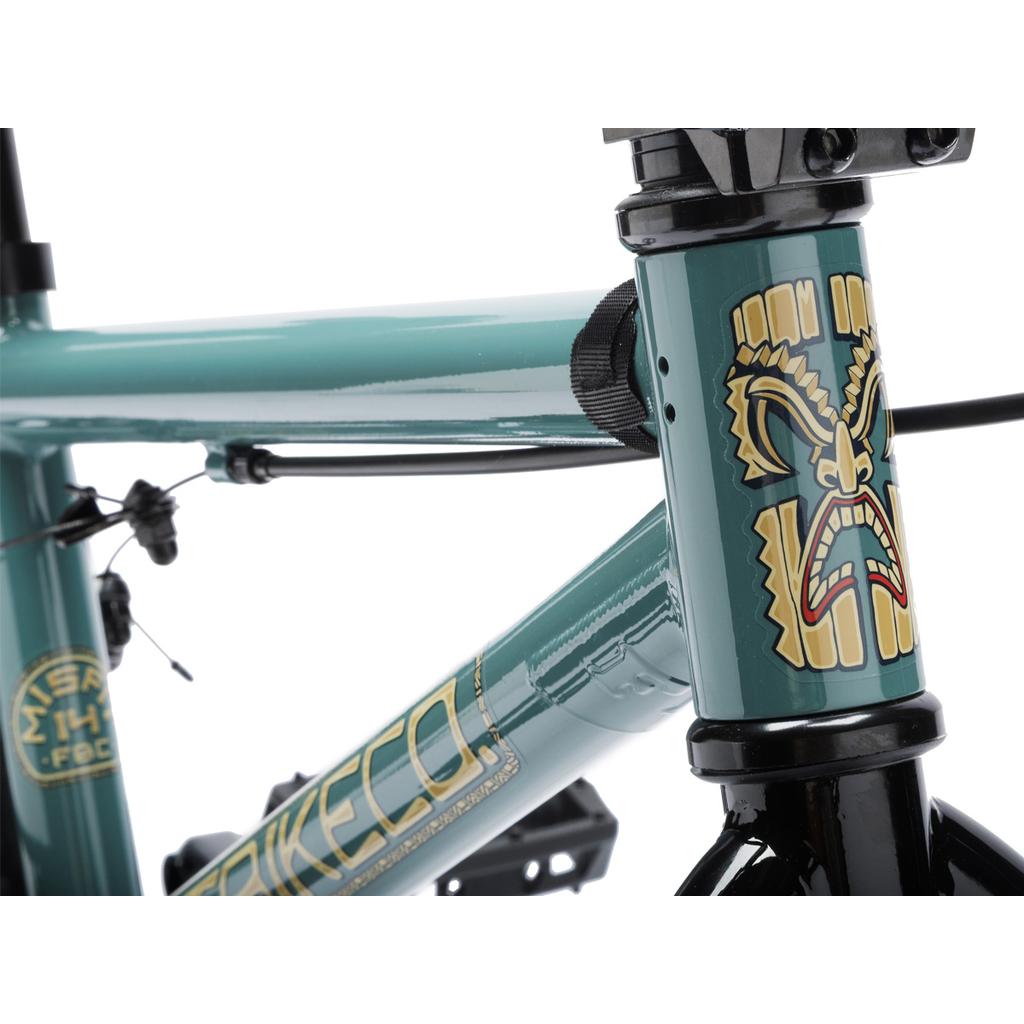 Close-up of the Fit Bike Co Misfit 14 Inch Bike in teal, showcasing a tiki face graphic near the handlebars with visible cables and a black fork—an ideal stylish BMX choice for young riders.