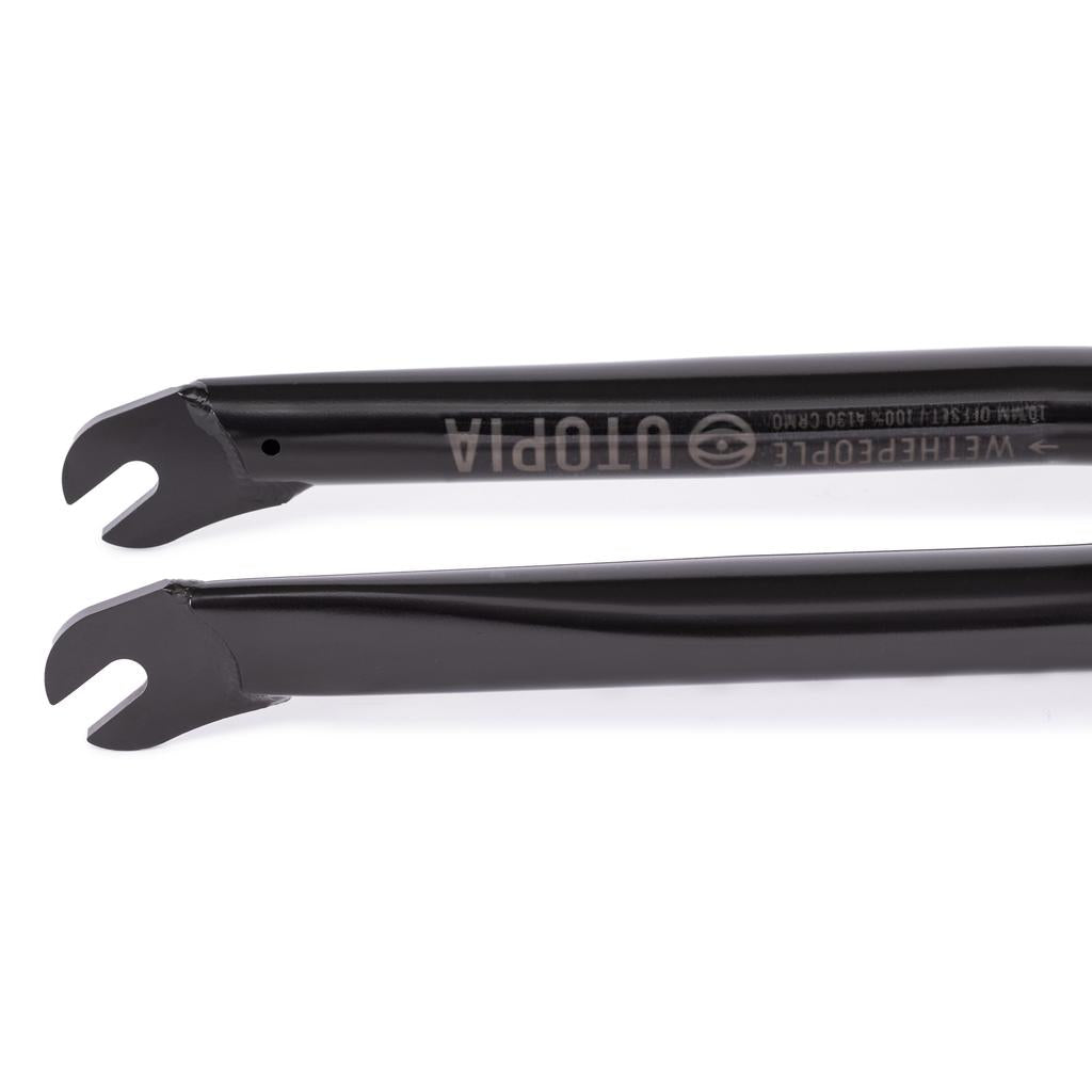 Close-up of two black Wethepeople Utopia Flatland Forks (10mm Offset) dropouts with cutouts, lying parallel on a white background—a lightweight BMX fork made for flatland riders.