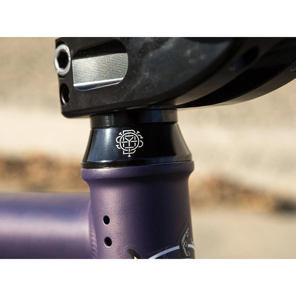 Close-up of the head tube and headset with a geometric logo on the matte purple Sunday Dark Wave Authentic 20 Inch Bike, featuring a 100% Chromoly frame.